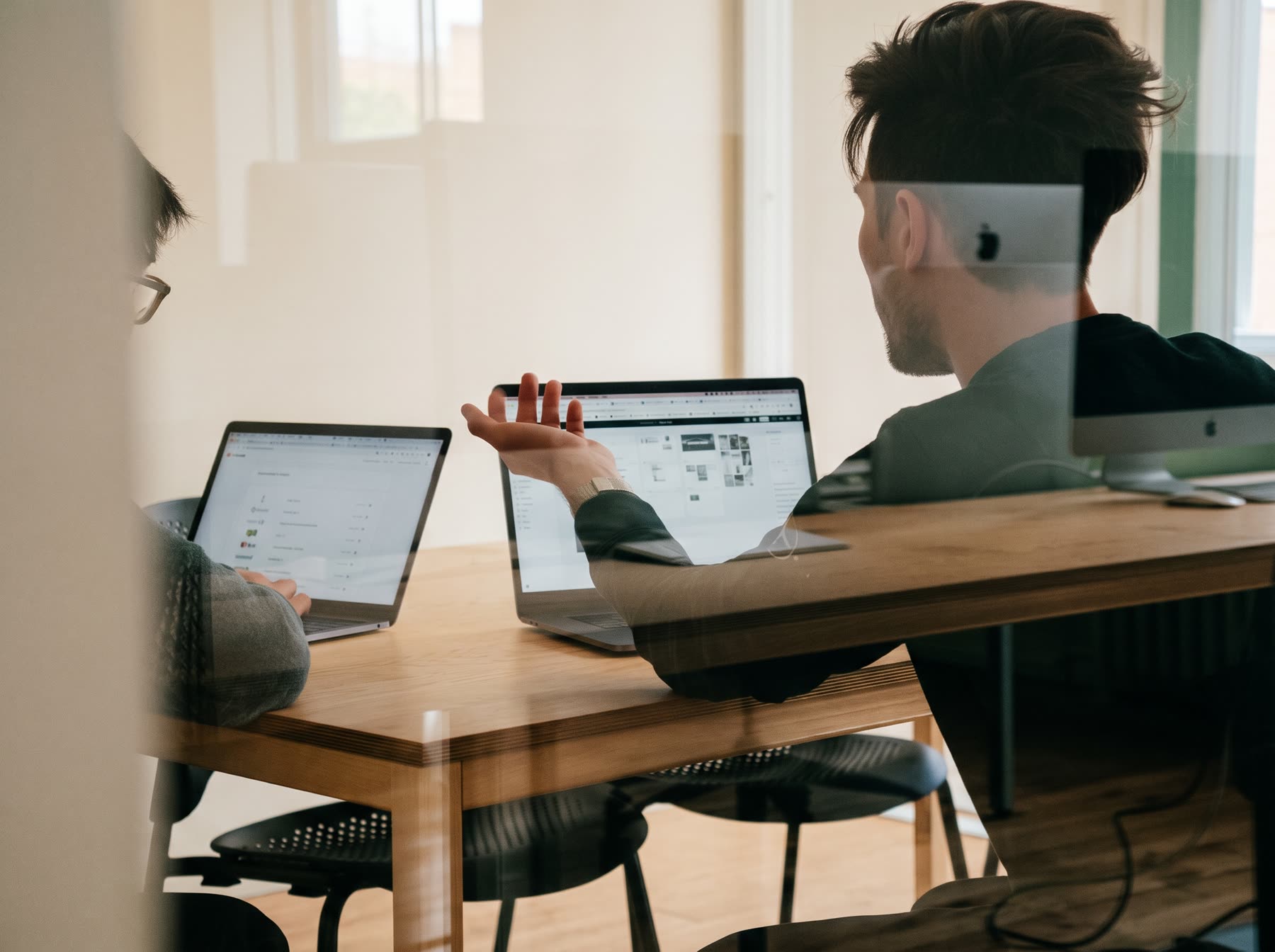 Two colleagues talking through their work at laptops in a sunlit office